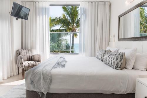 a white bedroom with a large bed and a window at On The Beach Noosa Resort in Noosa Heads