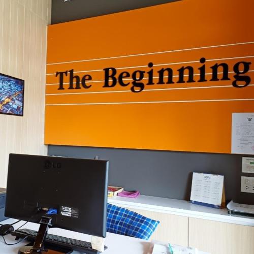 a desk with a computer in front of an orange sign at The Beginning Hotel in Betong
