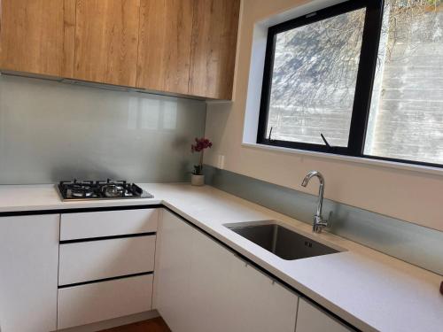 オークランドにあるNew Greenhithe Cozy Flatの白いキャビネット、シンク、窓付きのキッチン