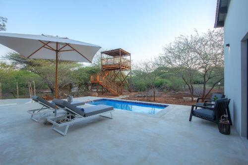 a swimming pool with two lounge chairs and an umbrella at Pillows Luxury Safari Villa, Wood-Fired Hottub, Giraffe-Feeding-Tower, Large Private Pool in Marloth Park
