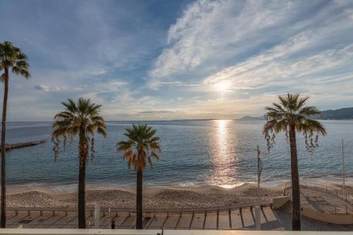un groupe de palmiers sur une plage avec l'océan dans l'établissement Le Soleil Front de Mer Centre Juan Les Pins, à Antibes