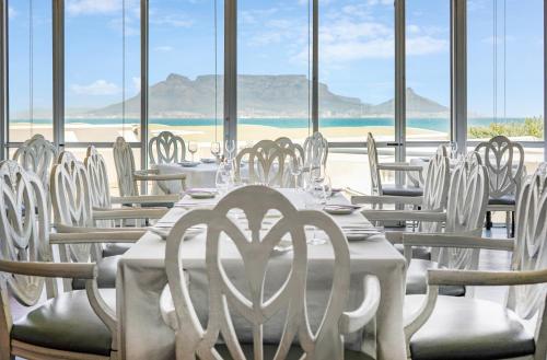 a dining room with white tables and chairs and the beach at Dolphin Beach Hotel Self Catering Apartments in Bloubergstrand