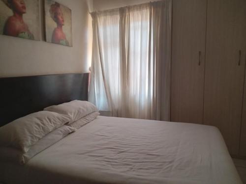 a bedroom with a bed with white sheets and a window at Vuya Nathi Bed and Breakfast in Manzini