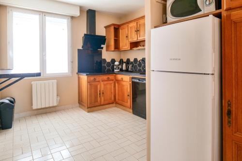 La cuisine est équipée d'un réfrigérateur blanc et de placards en bois. dans l'établissement Bel appartement 6 personnes - Quartier Arago, à Les Sables-dʼOlonne
