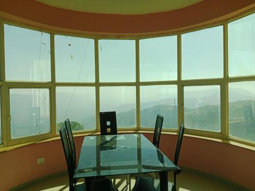 a table and chairs in a room with windows at Dev anand Villa in Mahabaleshwar