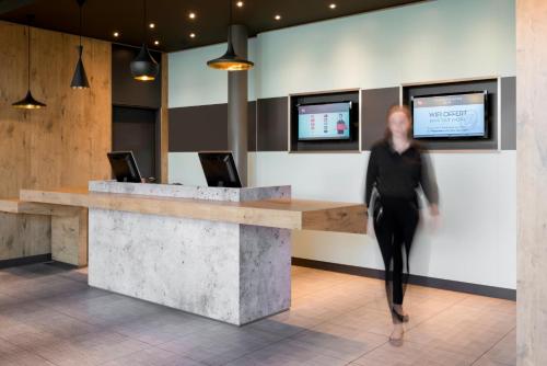 a woman walking past a reception desk in a lobby at ibis Genève Aéroport in Geneva