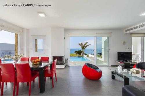 a living room with a table and red chairs and the ocean at BLUE CORAL BEACH VILLAS three exclusive villas - Poseidon - Nautilus - Oceanos - and - Baby Coral bungalow in Coral Bay