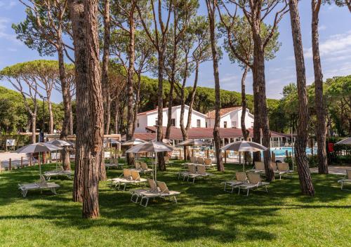 a group of chairs and umbrellas in a park with trees at Club del Sole Jesolo Family Resort in Lido di Jesolo