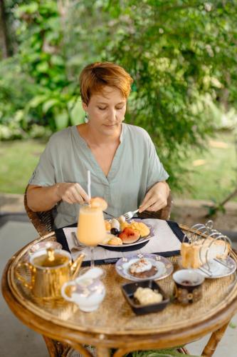 a woman sitting at a table with a plate of food at Emel's Retreat By Tropical Magnum - Luxury Boutique Villa in Anhandigoda