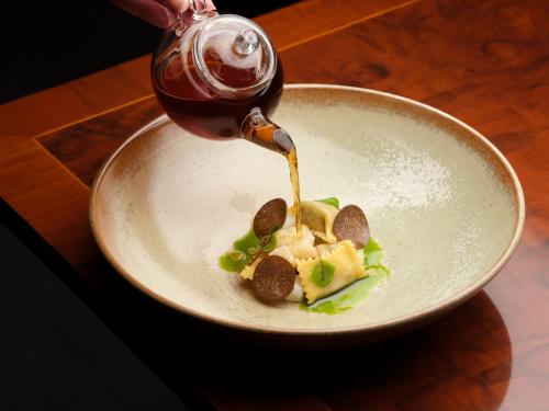 a person pouring sauce onto a plate of food at The Stafford London in London