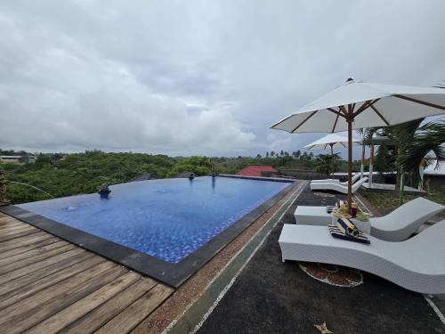 a swimming pool with two chairs and an umbrella at Kelingking BMS Penida Hills Villa in Nusa Penida