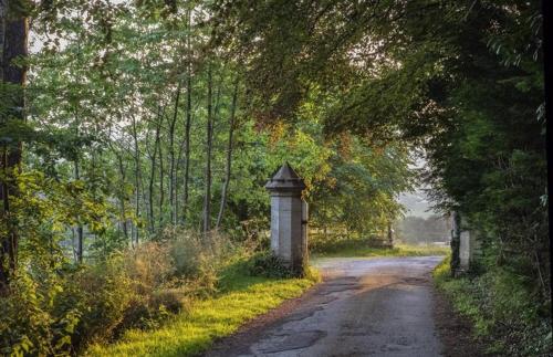 a dirt road with a stone pillar next to a fence at Hawkwood in Stroud