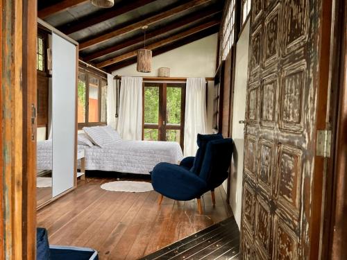 a living room with a blue chair and a bedroom at Casa Saíra in Bombinhas