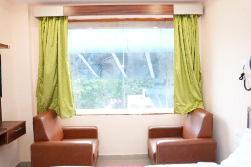 two chairs in front of a window with green curtains at Hotal Virinchi Ultra Comforts - Good Rooms - Brand New Building in Tirupati