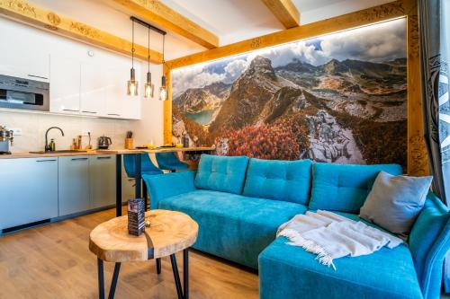 a living room with a blue couch and a kitchen at Euphoria Mountains by Apart Concept Podhale in Kościelisko