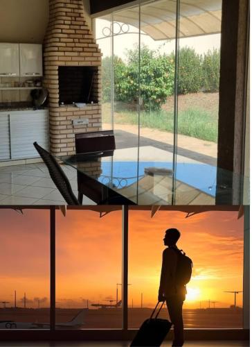 un uomo con una valigia che guarda fuori dalla finestra al tramonto di Casa Lins 15 pessoas temporada a Lins