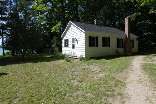 a small white house sitting in a field at Lakeside Cottage on Torch Lake in Alden