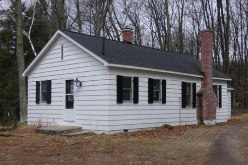 a white house with black windows and a brick chimney at Lakeside Cottage on Torch Lake in Alden