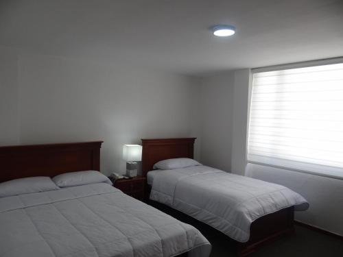 a bedroom with two beds and a window with a window shade at Altura Rooms & Suites in Quito