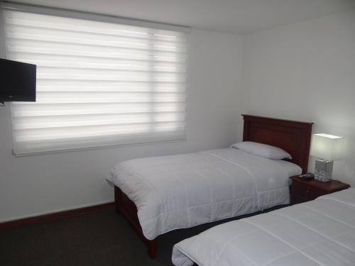 a bedroom with two beds and a window with blinds at Altura Rooms & Suites in Quito