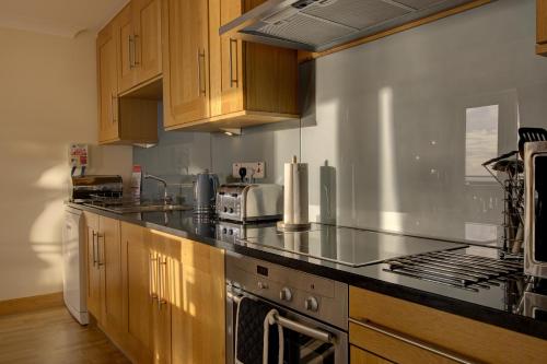 a kitchen with black counter tops and wooden cabinets at No10 The Links Apartment, Brora in Brora