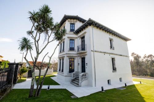 a white house with a palm tree in front of it at Indiano House Apartments, Muros de Nalón, 5km Cudillero in Muros de Nalón