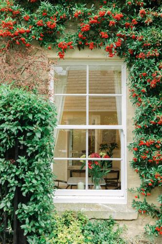 a window with red flowers on the side of a building at Cotteswold House in Bibury