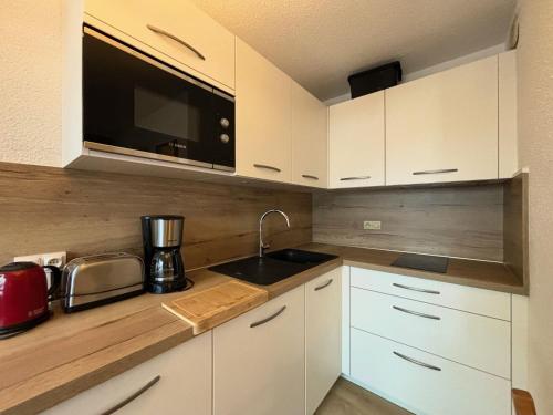 une cuisine avec des armoires blanches, un évier et un micro-ondes dans l'établissement Studio 4 pers, pied des pistes, Les Ménuires - Balcon sud, proche commerces et école de ski - FR-1-452-52, aux Menuires