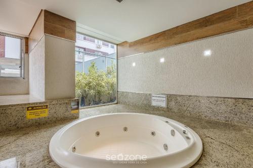 a large bath tub in a bathroom with a window at Lindos Estúdios em Condomínio c/ Piscina - Águas Claras - MADB in Águas Claras