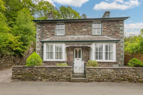 a brick house with a white door and a stone wall at Rockwood- Grasmere family cottage with Hot tub in Grasmere