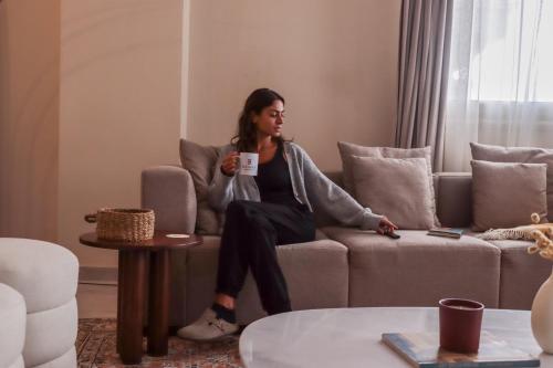 a woman sitting on a couch holding a cup of coffee at VIDA by Elegant Hospitality in Cairo