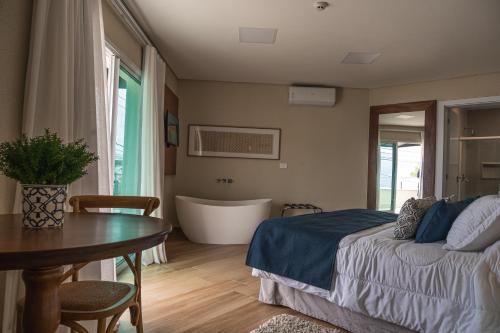 a bedroom with a bed and a table and a tub at Hotel VillaReal Charme in Guaratuba