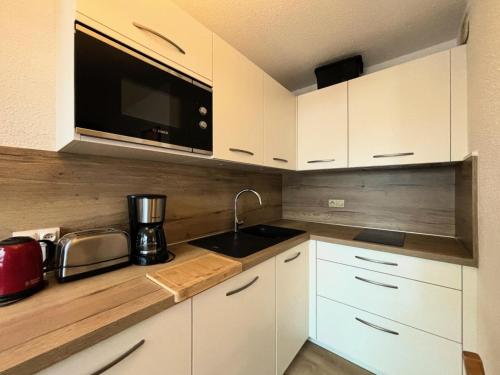 une cuisine avec des armoires blanches, un évier et un micro-ondes dans l'établissement Résidence Carlines I - Studio 4 personnes au pied des pistes aux Ménuires MAE-5694, aux Menuires