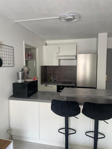 une cuisine avec des placards blancs et deux tabourets de bar noirs dans l'établissement Le soleil Niçois, proche du port, à Nice