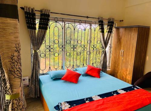a bed with red and blue pillows in front of a window at The Bodhi Tree Resort in Morjim