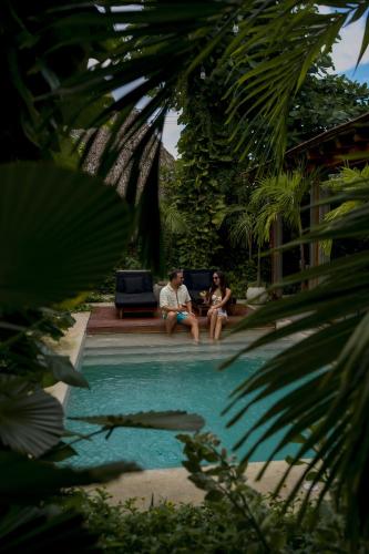 two people sitting on a bench next to a swimming pool at Colonte Hotel Origen in Valladolid