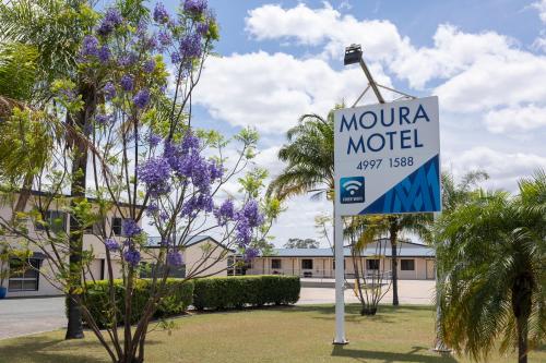 a motel sign in front of a building with purple flowers at Moura Motel in Moura