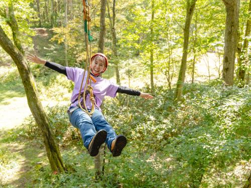 a young girl is jumping on a rope in the woods at Labo Land Kurohime in Shinano