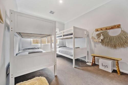 a white bedroom with two bunk beds and a mirror at Tea Tree Retreat - 5 Bedrooms, sleeps 13 in Inverloch