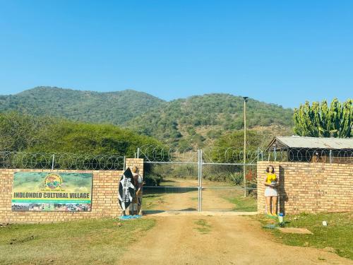 une femme debout à côté d'un mur de briques avec une clôture dans l'établissement Indlondlo Cultural Village, à Cato Ridge