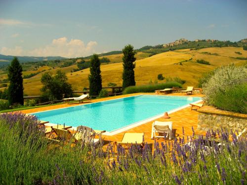 a large swimming pool with chairs and a hill at Agriturismo Poggio Istiano in Bagno Vignoni