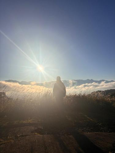 a man standing in a field with the sun in the sky at Guesthouse HOALOHA 4 SEASONS in Chino