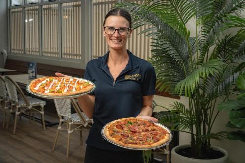 a woman is holding two pizzas in a room at The Belmont Hotel in Belmont