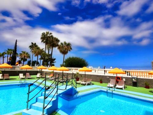 a swimming pool with orange umbrellas and chairs at PaulMarie Olympia Studio in Playa de las Americas