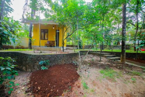 a yellow house with a stone wall and trees at Green Waters Resort by Aradhana Leisure in Embilipitiya