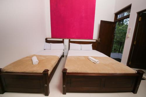 two twin beds in a room with a pink wall at Green Waters Resort by Aradhana Leisure in Embilipitiya