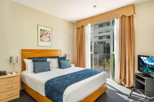 a bedroom with a bed and a tv and a window at Ramada by Wyndham, Hamilton City Center in Hamilton