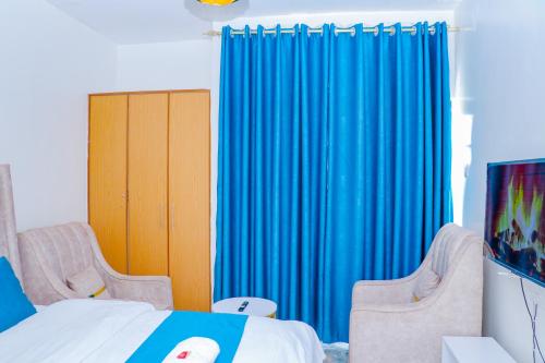 a bedroom with blue curtains and a bed with two chairs at Haydenco Suites Signatuture Mall Syokimau in Nairobi