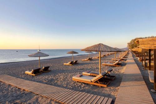 a group of lounge chairs and umbrellas on a beach at Lindian Village All Inclusive Resort Rhodes,Curio Collection in Kiotari