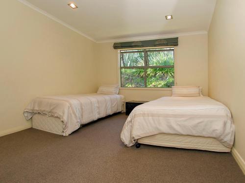 two beds in a room with a window at Cooks Getaway - Cooks Beach Holiday Home in Cooks Beach